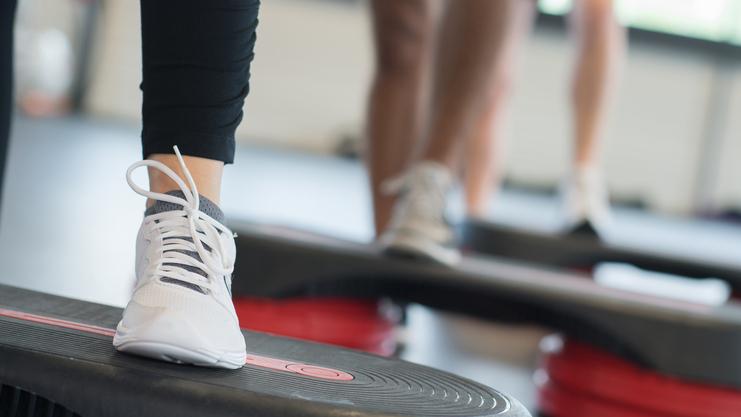 Nahaufnahme eines Fußs mit einem weißen Sport-Schuh auf einer Fitness-Stepp-Platte während eines Workout.