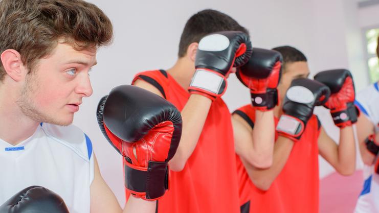 Vier junge Boxer in Trainingshaltung, bereit für das Training, tragen farbige Boxhandschuhe und Sportkleidung.