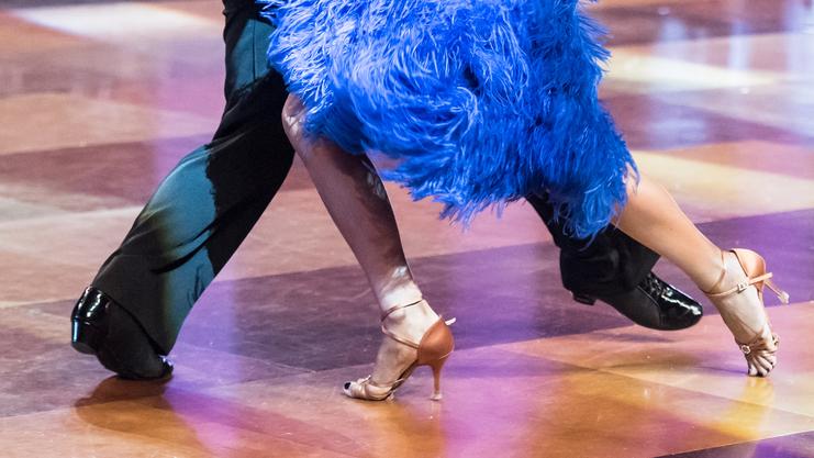 Tanzpaar in Bewegung, der Fokus liegt auf den Füßen der Tänzer und dem auffälligen blauen Kleid mit Federn.
